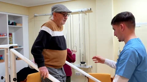 Elderly man practicing walking with physiotherapist support in nursing home Stock Footage 307593148