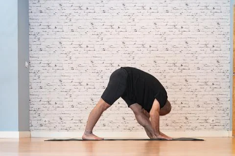 Elderly man practicing a yoga forward bend on a mat in a bright, spacious room. Stock Photos