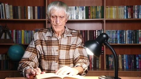 Elderly man reading book in library turning pages. Video stock 169090679