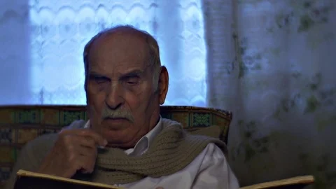 Elderly Man Reading Book Licks Finger Turns Page Man is Resting in Comfortable Stock Footage 72229007