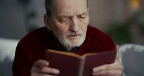 Elderly man reading a book in a quiet softly lit indoor setting Stockbeeldmateriaal 336288674