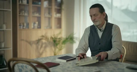Elderly man reading papers at a dining table in a bright home interior Stock Footage 336281070