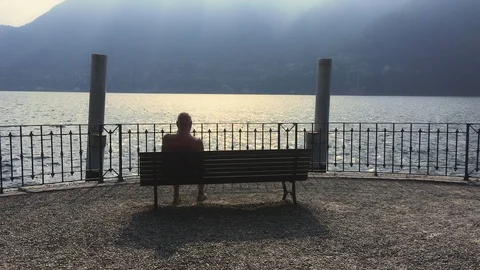 Elderly man rests on a bench on the como lake with Passing ship Stock Footage 118649883