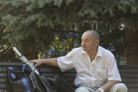 An elderly man sat down on a bench to relax in a park among trees and flowers Stock Photos