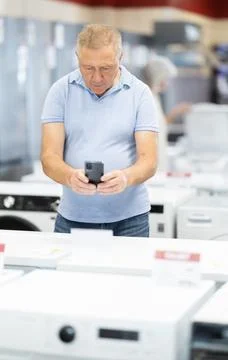 Elderly man scanning QR-code on washing machine at household appliances store Stock Photos