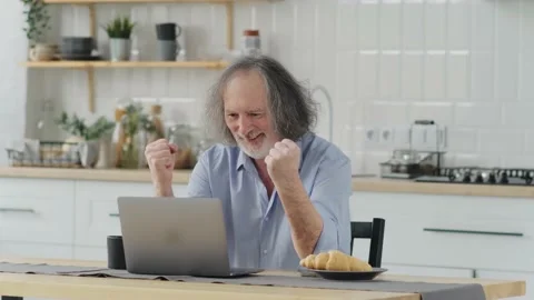 Elderly man seated on couch looking at laptop screen scream with joy feels Stock Footage 237628188