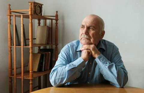 Elderly man seated at a table thinking Stock-Fotos
