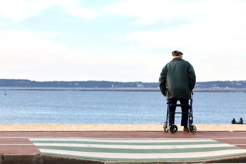 Elderly man siiting on walker looking out over beach Stock Photos