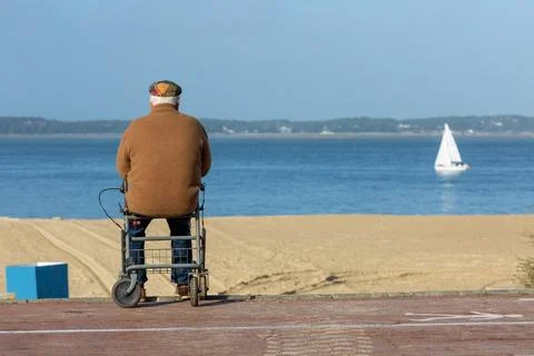 Elderly man siiting on walker looking out over beach Stock Photos