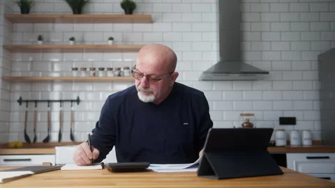 Elderly man sit in the kitchen using tablet device, study financial papers .. Stock Footage 269933065