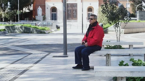 An elderly Man sits on a bench in the square talks on the phone Stock Footage 100952986