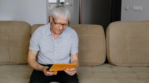 An elderly man sits on a couch and examines old photos. Good memories. Stockbeeldmateriaal 111141831
