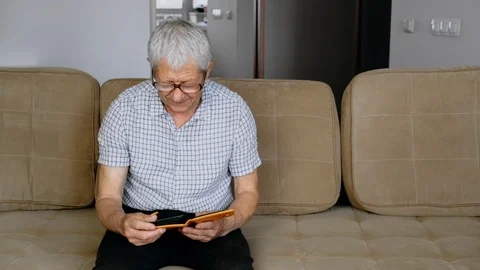 An elderly man sits on a couch and examines old photos. Good memories. Stockbeeldmateriaal 111142032