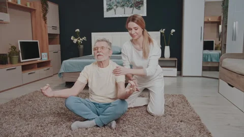 Elderly man sits in the lotus position at home with instructor 스톡 동영상 328025734