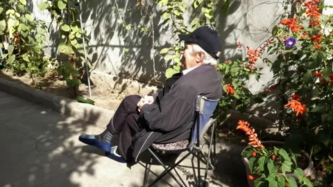 An elderly man sits on an old folding chair in his yard. Vídeos de archivo 162958649