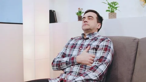 An elderly man sits on the sofa, experiencing heart pain, stroke or heart attack Stock-Footage 301575159