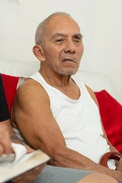 An elderly man sits on a sofa looking to the side with a serious face, a gr.. Фото