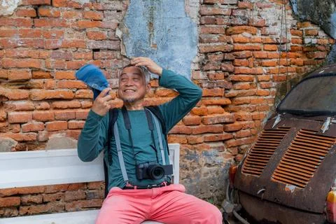 Elderly man sitting on bench with camera in front of old brick wall and vin.. Stock Photos