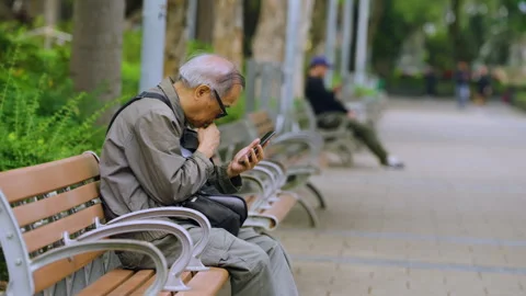 Elderly Man Sitting On A Park Bench And Using His Mobile Phone. - wide shot Stock Footage 337195745