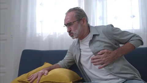 Elderly man sitting on a sofa and holding his chest in pain Stock Footage 326179711