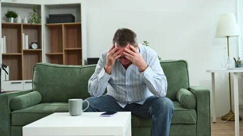 Elderly man sitting on sofa, holding head in hands, showing stress, depress.. Stock Footage 312852553