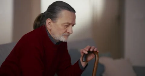 Elderly man sitting on sofa in profile with thoughtful expression indoors 動画素材 336279104