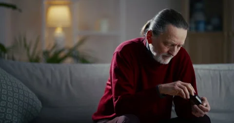 Elderly man sitting on sofa using smartphone in a cozy living room Vídeo Stock 336287804