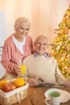 Elderly man sitting at the table while his wife giving him orange juice Stock Photos