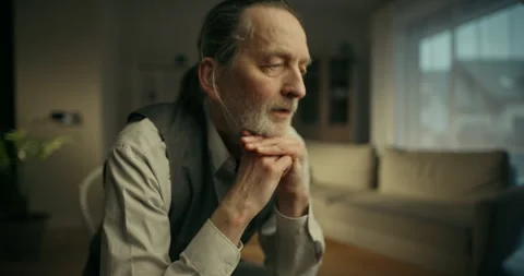 Elderly man sitting by a window in soft natural light Видео 336277849