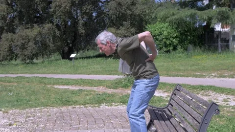 Elderly man standing from bench feels sudden back pain hernia Stock Footage 333194831