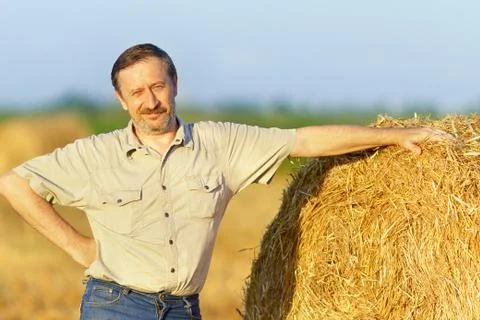 An elderly man is standing next to a stack of straw Stock Photos