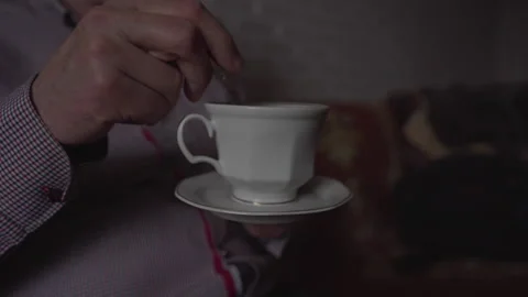 Elderly man stirs tea in ceramic teacup using small teaspoon 스톡 동영상 243646195