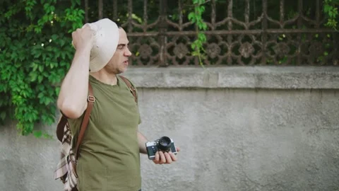 An elderly man stops next to a textured stone wall covered in green foliage Stock Footage 301107233