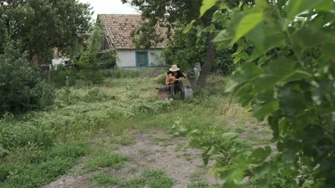 Elderly man in straw hat plays guitar near village house Video stock 201303473