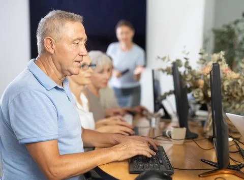 Elderly man taking computer lessons with group of elderly people in nursing home Stock Photos