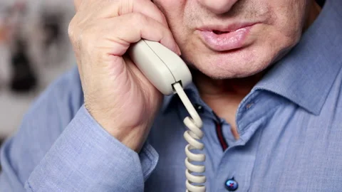 An Elderly Man Is Talking On A White Wired Phone In The Office, Holding The Phon 스톡 동영상 147403235