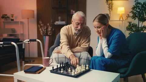 Elderly man teaching his young female carer to play chess game, having fun Stock Footage 279177389