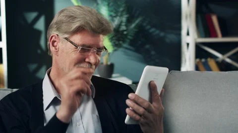 An elderly man tired of reading on a tablet is taking off glasses, rubbing his 库存影片 132635245