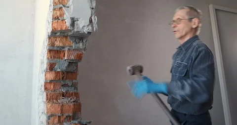 Elderly man trying to tear down wall, striking with large sledgehammer, breaking Stock Footage 124296068