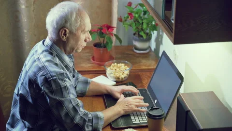 Elderly man typing on a keyboard working on a laptop at home in the evening Stock Footage 130345785