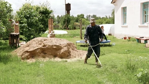 Elderly man in uniform mows grass on a plot near the house Stock Footage 132404924