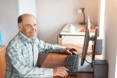 Elderly man using computer at home at the table Stock Photos