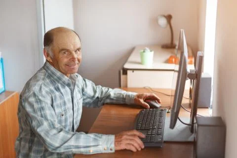 Elderly man using computer at home at the table Stock Photos