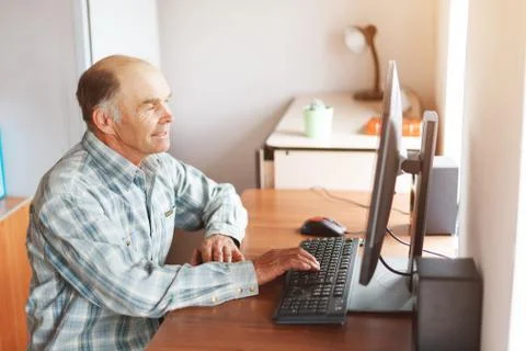 Elderly man using computer at home at the table Stock Photos