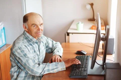 Elderly man using computer at home at the table Stock Photos