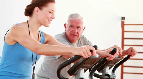 Elderly man using the exercise bike with his trainer Video stock 34130726