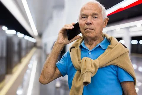 Elderly man using mobile phone while waiting for train in platform of Foto stock
