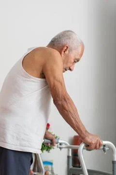 Elderly man using walker for mobility support while moving carefully inside.. Фото