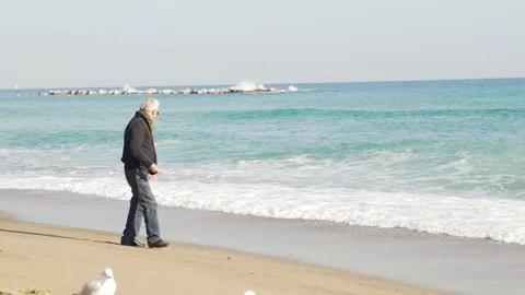Elderly man walking along the beach near the sea and feeding the seagulls Stock Footage 101269371