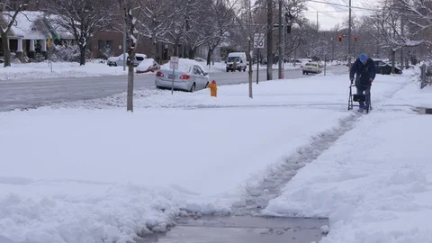 Elderly man walks down snow covered street with walker. Wide 스톡 동영상 86750707